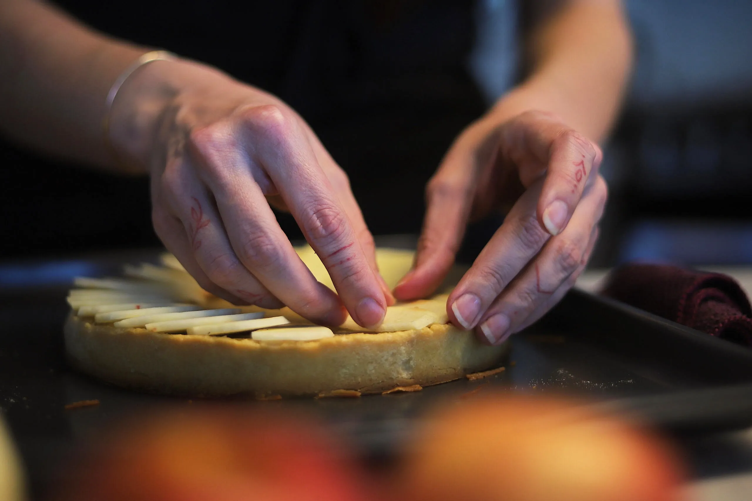 Aura Danton's hands arranging thinly sliced fruit on a tart shell