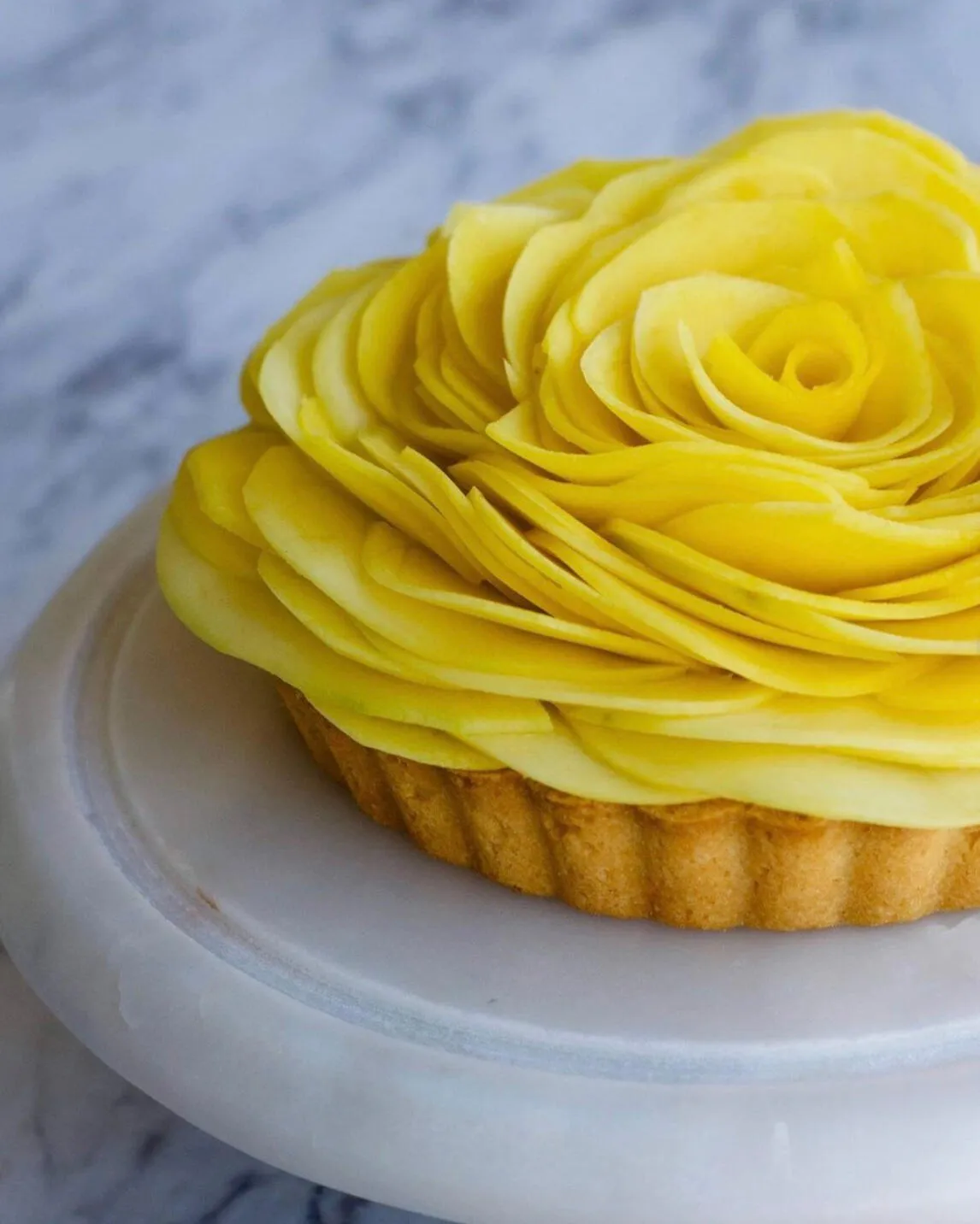 Tart topped with a rose of thinly sliced yellow fruit