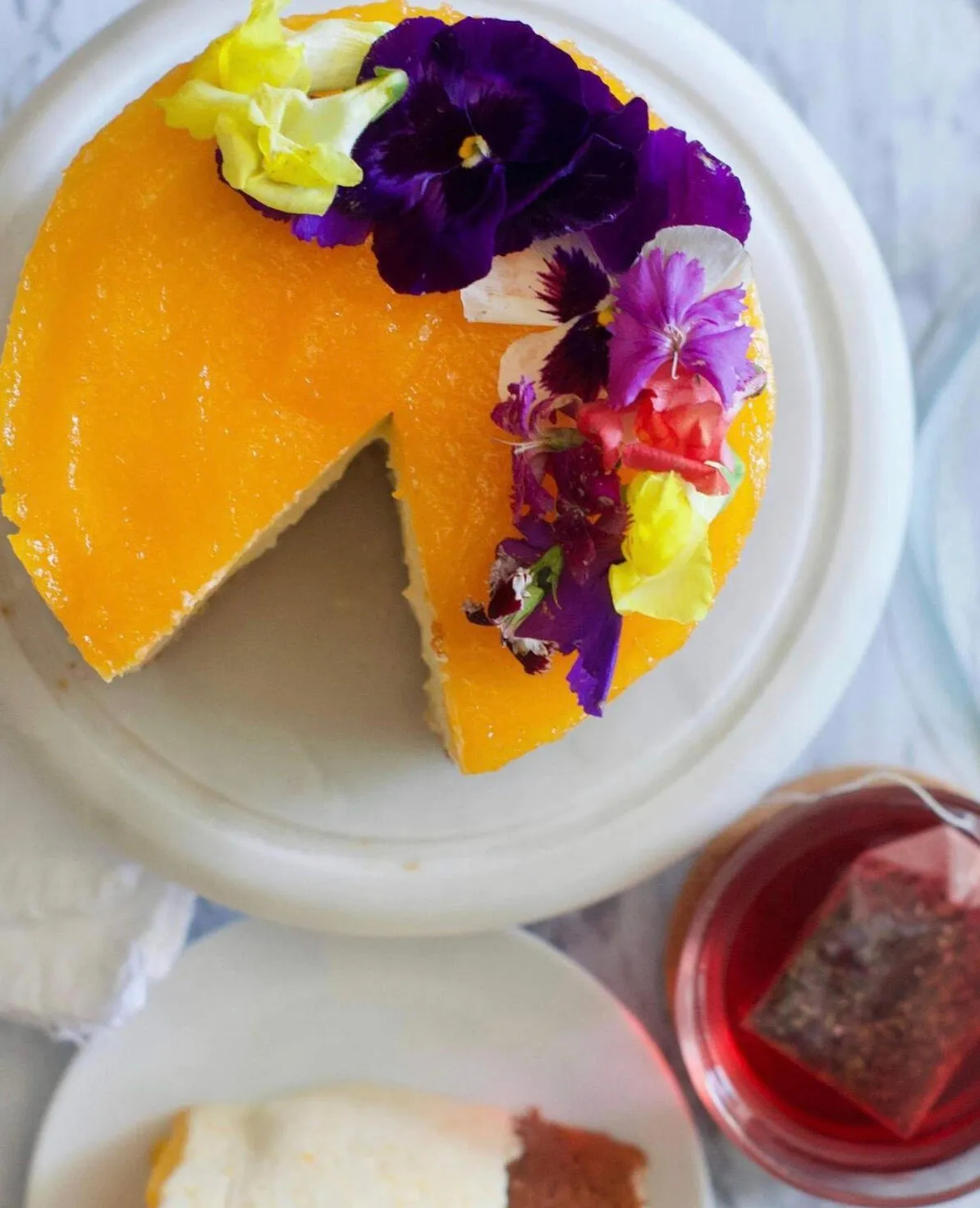 Glazed cake decorated with edible flowers, served with tea
