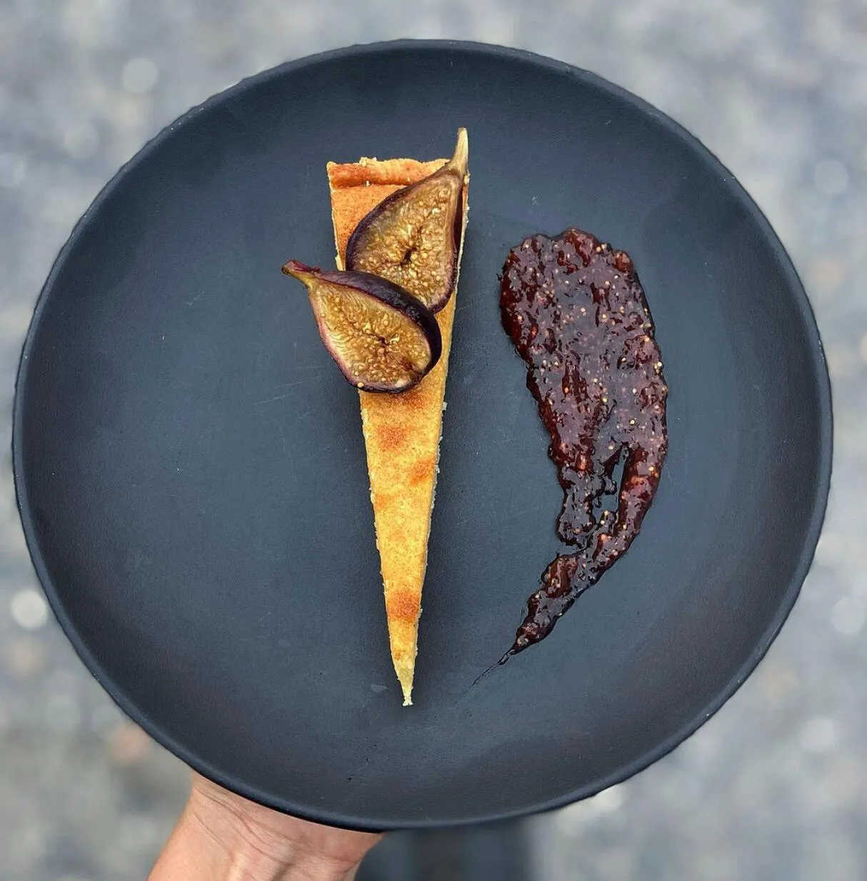 Slice of tart with fresh figs and a swipe of fig jam on a black plate