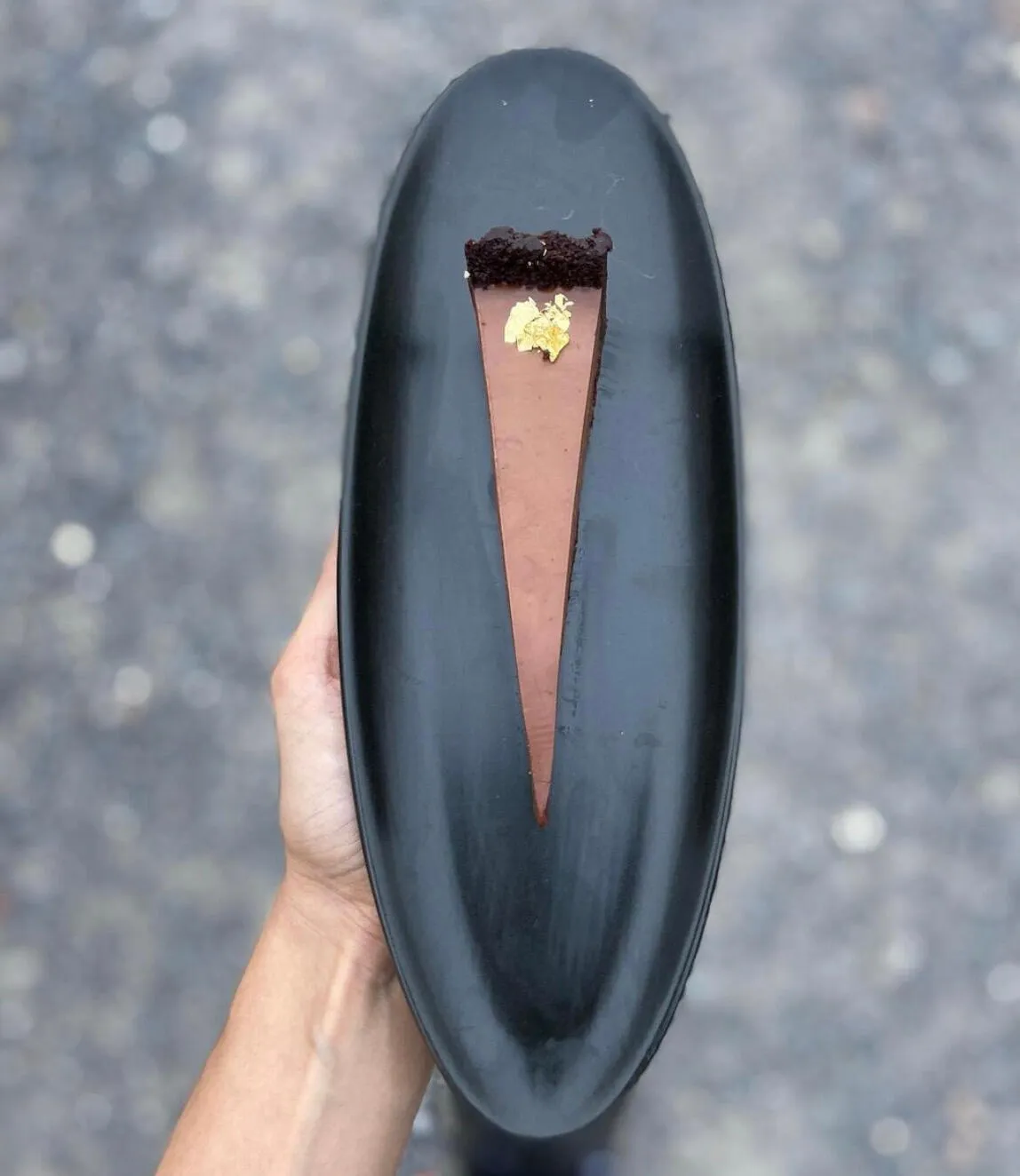 Narrow chocolate tart with gold leaf on a long black plate